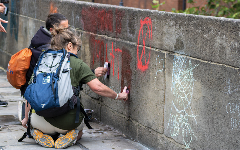 Two workers cleaning graffiti off of a wall