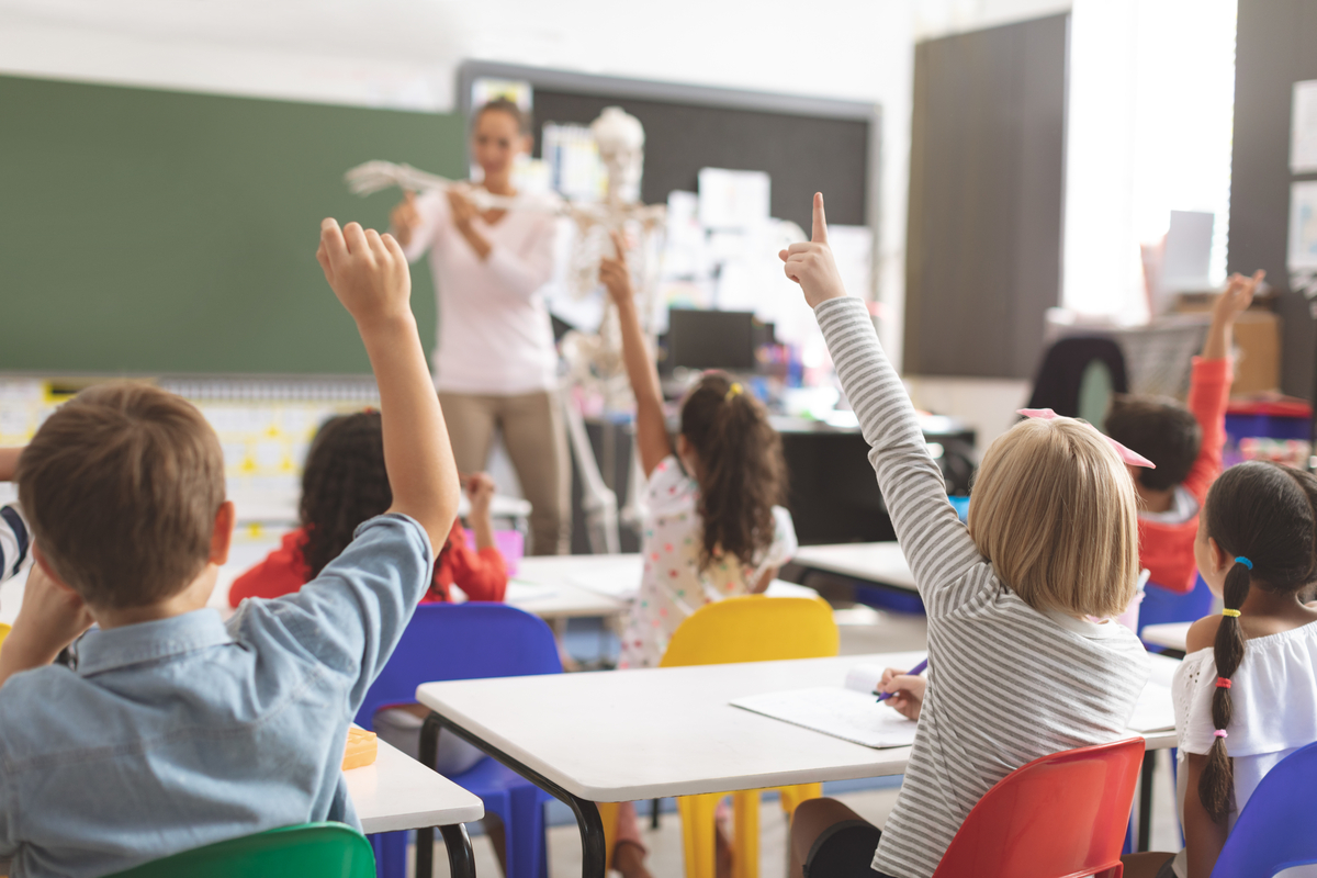 How to Keep Your Classroom Clean concept - teacher in front of a classroom with kids raising hands