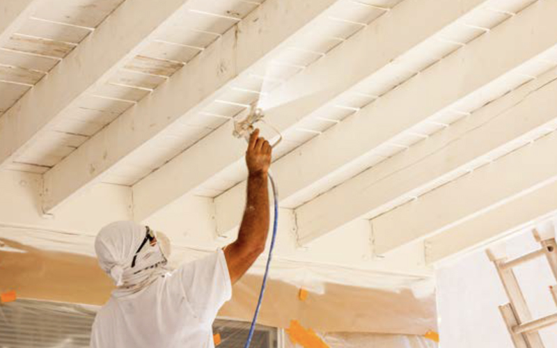 Worker spraying exposed wood ceiling